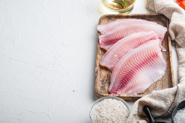 Tilapia di pesce bianco crudo, con ingredienti di riso basmati e pomodorini, su tavolo bianco, vista dall'alto