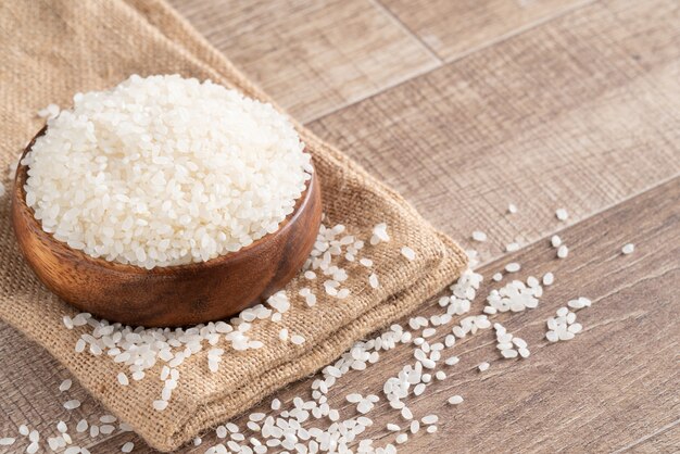 Raw white polished milled edible rice on wooden table background in a bowl, organic design concept.