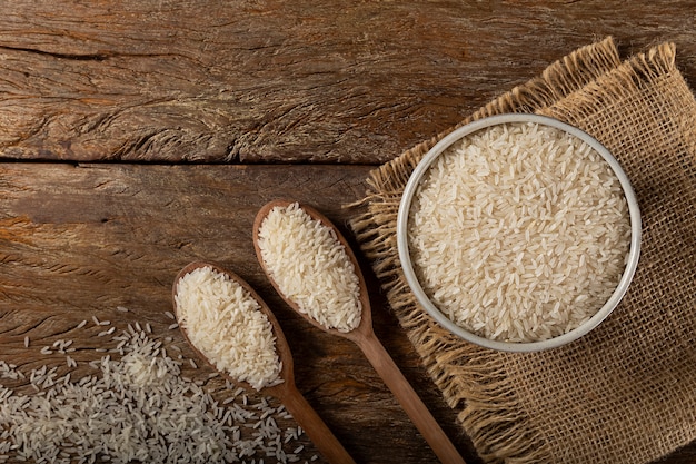 Raw white rice in a ceramic bowl on brown wooden background