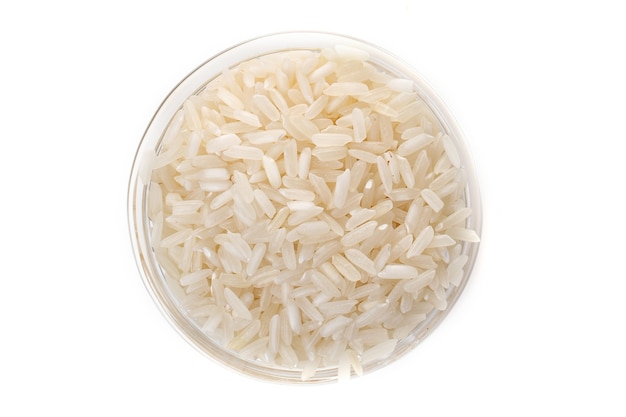 Сырой белый рис в прозрачной стеклянной пластине на белом фоне.