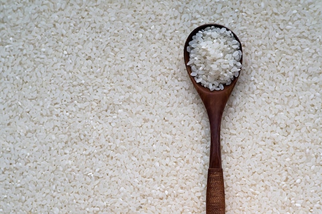 Raw white rice in spoon on wooden background