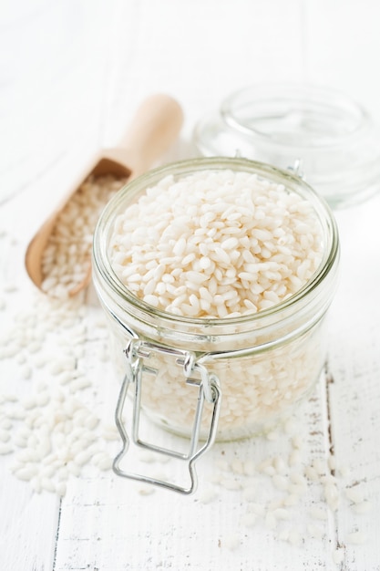 Raw White rice variety Arborio for Italian risotto dishes in glass jar on white concrete or stone background