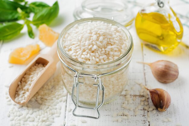 Raw White rice variety Arborio for Italian risotto dishes in glass jar on white concrete or stone background.