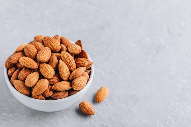 Raw whole almond in bowl on gray background Copy space