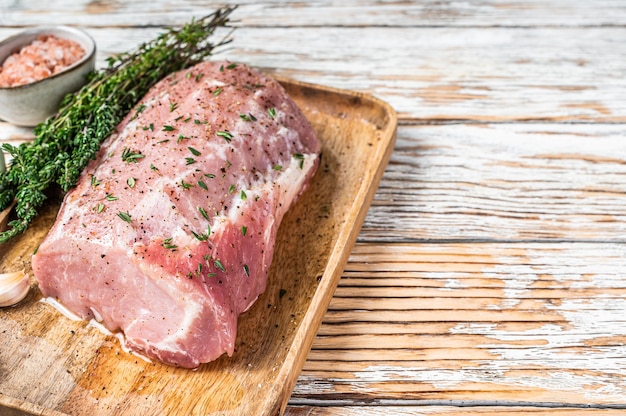 Carne di lombo di maiale intero disossato crudo con timo e sale su tavola rustica. fondo in legno bianco. vista dall'alto. copia spazio.