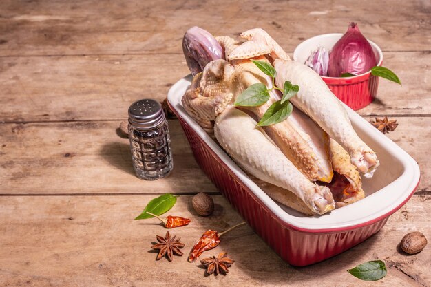 Raw whole chicken carcass for healthy food lifestyle. Free-range farm bird with traditional Chinese spices in ceramic baking pan. A trendy hard light, dark shadow, vintage wooden table, copy space