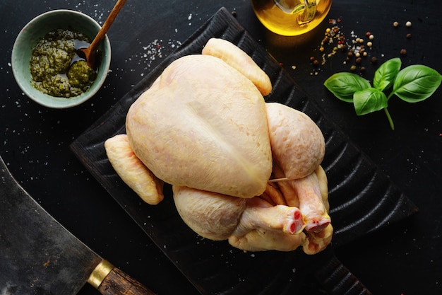 Raw whole corn chicken with spices on dark table