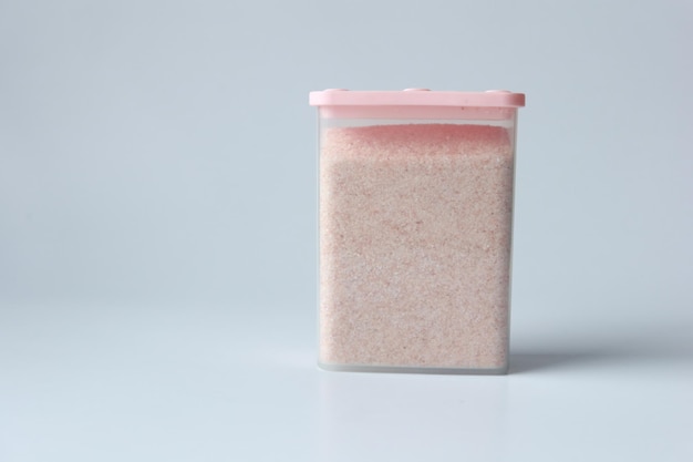 Raw whole dried pink Himalayan salt in a container on white