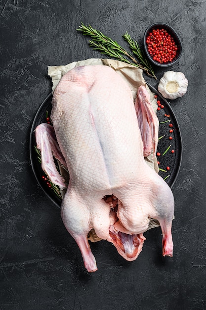 Raw whole duck, pink pepper and rosemary. Black background. Top view