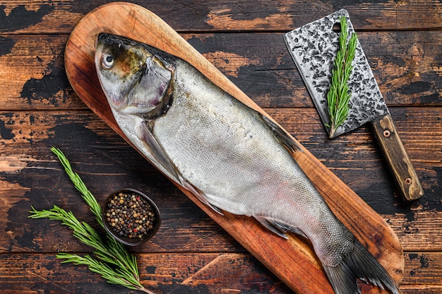 Raw whole fish silver carp on a cutting board with rosemary. Dark . 