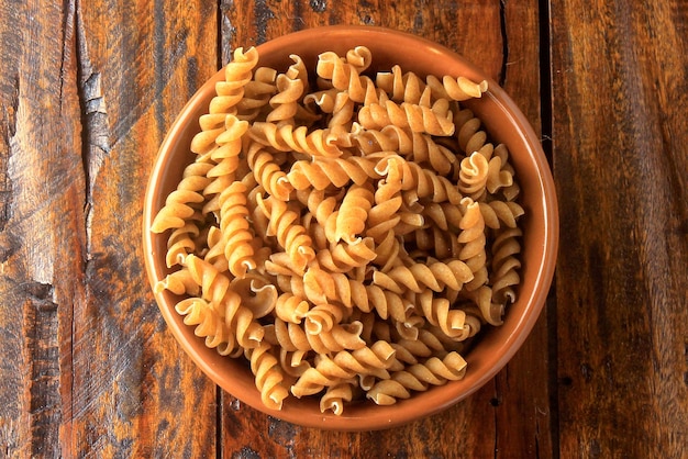 Raw whole grain fusilli pasta in bowl on rustic wooden kitchen table