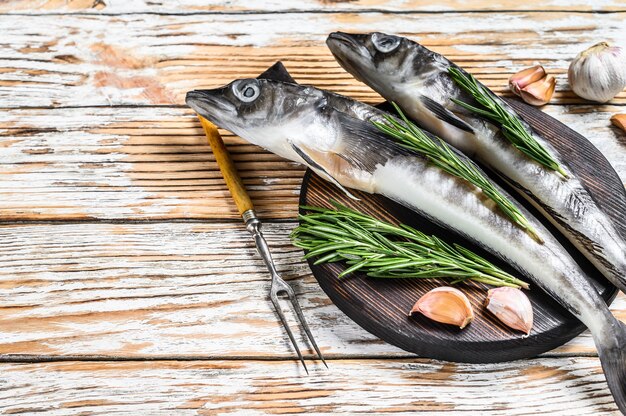 Raw whole icefish with herbs. White Wooden background. Top view. Copy space.