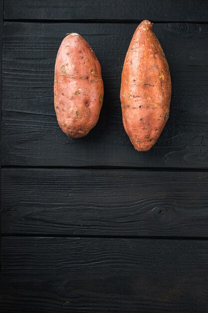 Raw whole sweet potatoe, on black wooden background, flat lay with copyspace.