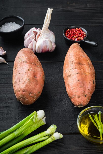 Raw whole sweet potatoe  with ingredients, on black wooden background.