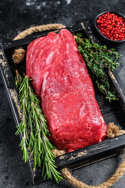 Carne di vitello intero filetto crudo su un vassoio di legno con erbe aromatiche.