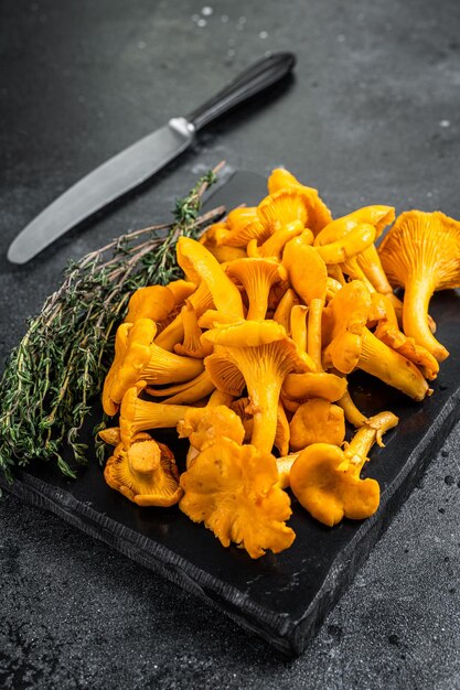 Raw wild Chanterelles mushrooms on a marble board. Black background. Top view.