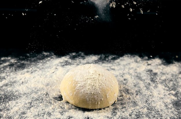 Raw yeast dough sprinkled with flour on a black background Dough for making bread or pizza