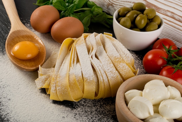 Raw yellow italian pasta pappardelle, fettuccine or tagliatelle close up with eggs.