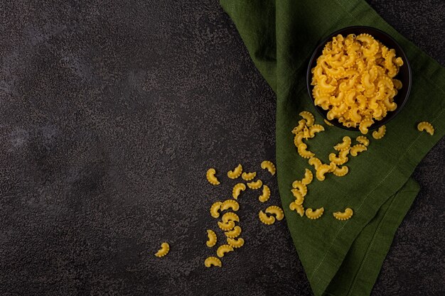 Raw yellow pasta in a small bowl on a dark structural background with space to copy. top view. Copyspace