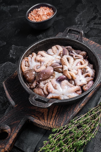 Raw young baby octopus in a skillet ready for cooking Black background Top view