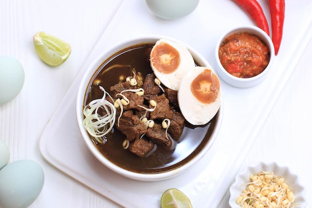 Rawon, Indonesische Traditionele Beff Zwarte Soep uit Oost-Java. Geserveerd op een kom met garnalencracker (kerupuk Udang) en chilipasta en gezouten ei