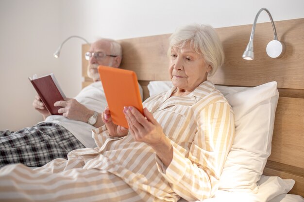 Reading. Aged married couple lying in bed and reading