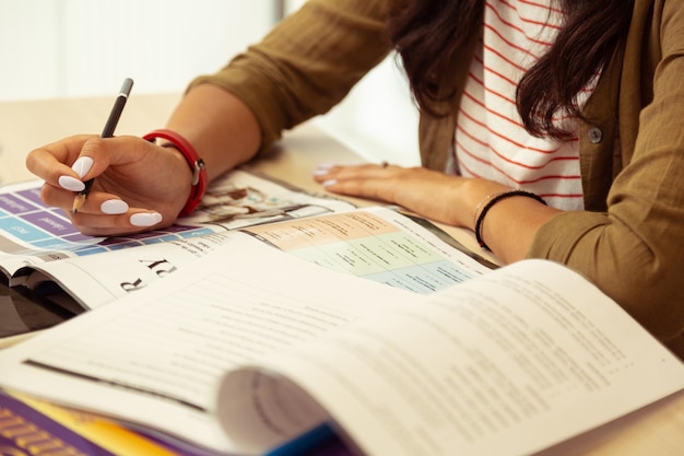 Reading book. Close up of motivated girl that leaning elbows on table while doing test