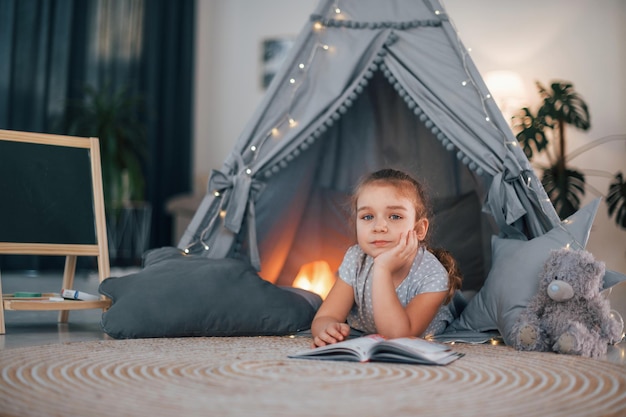 reading the book cute little girl playing in the tent that is in the domestic room