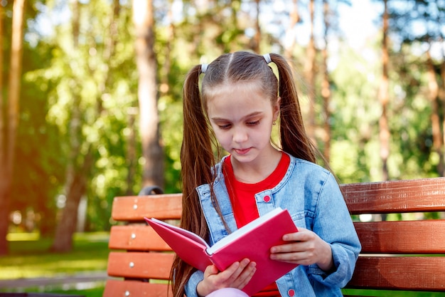 本を屋外で読む。本を読んで、ベンチに座っている十代の少女。