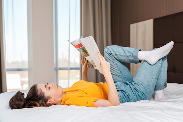 Reading and education A woman reads a magazine lying on the bed Indoor Side view