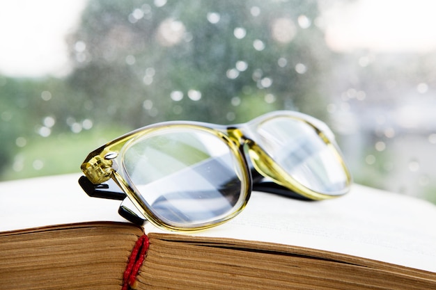 Reading glasses and book on rainy window