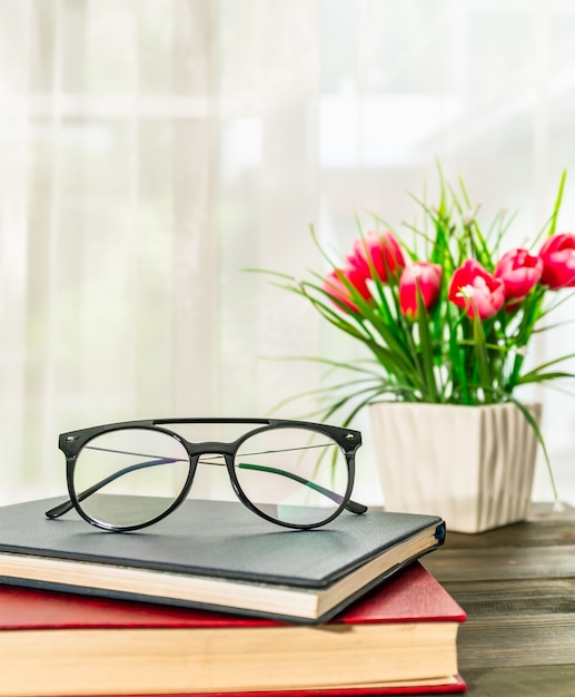 Reading glasses put on hardcover books over wooden table beside the window