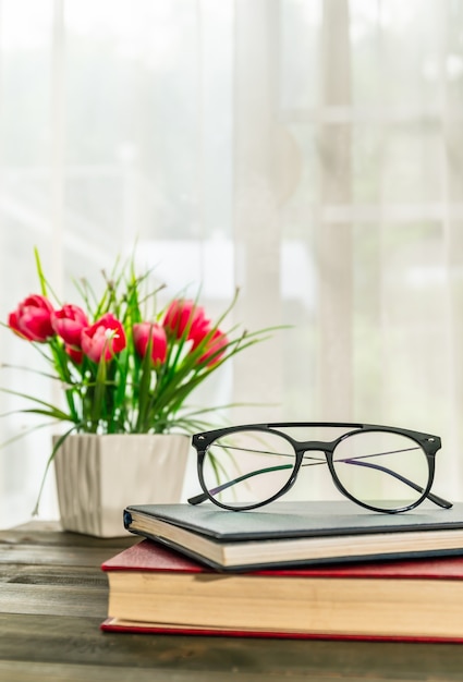 Reading glasses put on hardcover books over wooden table beside the window