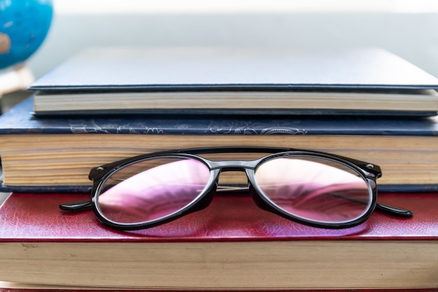 Reading glasses put on hardcover books over wooden table