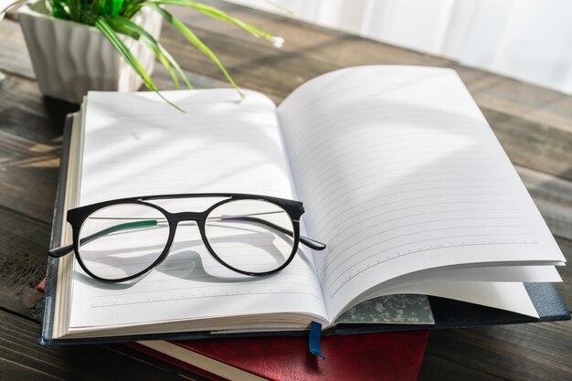 Reading glasses put on open book over wooden table