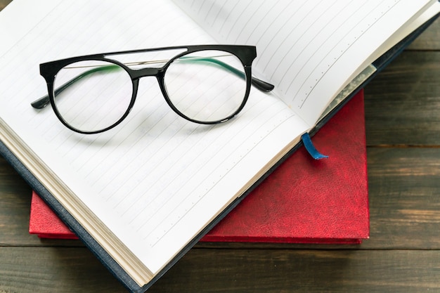 Reading glasses put on open book over wooden table