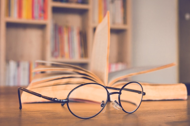 Reading glasses on table with book and book case background