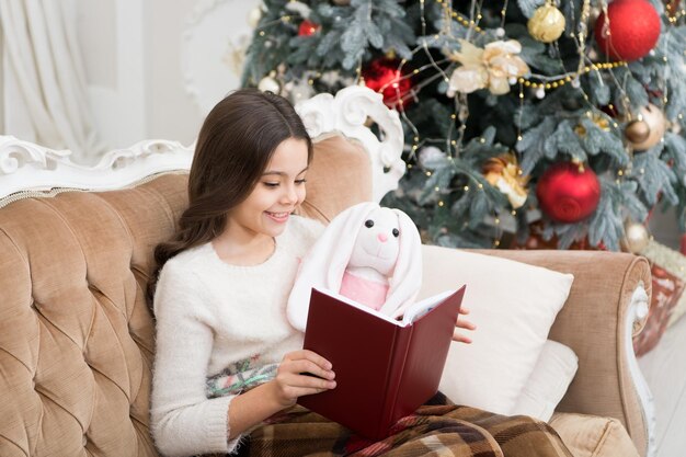 Leggere è sempre una buona idea la bambina legge il libro per un amico giocattolo il bambino piccolo si diverte a leggere la storia di natale lettura invernale all'albero di natale elenco di letture per le vacanze