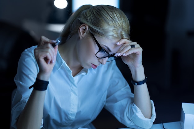 Reading new material. Diligent concentrated young woman sitting in the office and reading documents while working on the project and taking notes