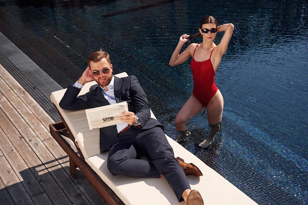 Photo reading the newspaper man with woman is in the pool together