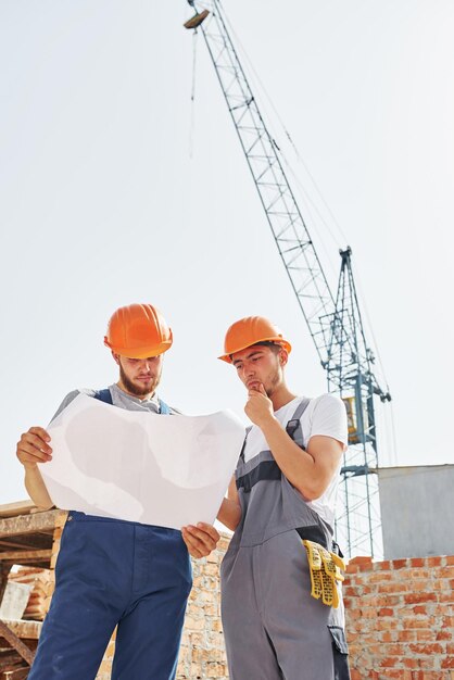 Reading plan Two young construction workers in uniforms is busy at the unfinished building