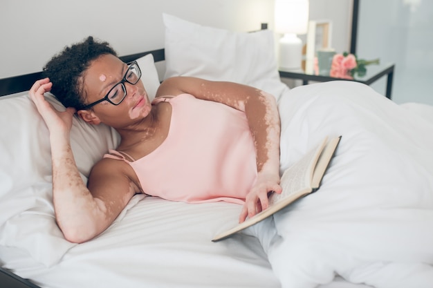 Reading. a young woman in eyeglasses reading a book while laying in bed