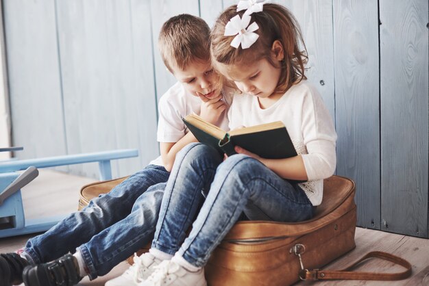 Ready to big travel. Happy little girl and boy reading interesting book carrying a big briefcase. Freedom and imagination concept