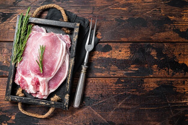 Ready for cooking raw pork chop steaks in a wooden tray with rosemary Wooden background Top view Copy space