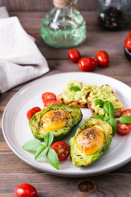 Ready-to-eat appetizer baked avocado with egg, toast and cherry tomatoes on a plate on a wooden table. Healthy eating. Flexitarian diet. Vertical view