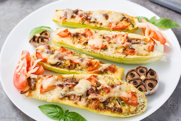 Ready-to-eat baked zucchini halves stuffed with cheese and tomato and basil leaves on a plate on the table. Vegetable dishes, healthy food. Close-up