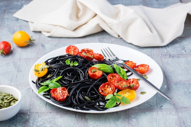 Ready to eat black spaghetti with dried tomatoes, sesame seeds and pumpkin on a plate on the table. gourmet food