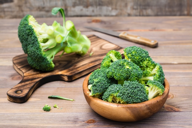 Ready to eat fresh raw broccoli is divided into inflorescences in a wooden plate and on a cutting board and a knife on a wooden table.