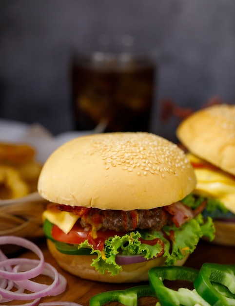 自家製ハンバーガーと新鮮な食材をバックグラウンドでグラス一杯の飲み物と一緒に食べる準備ができています。ダークスタイルの光で撮影。