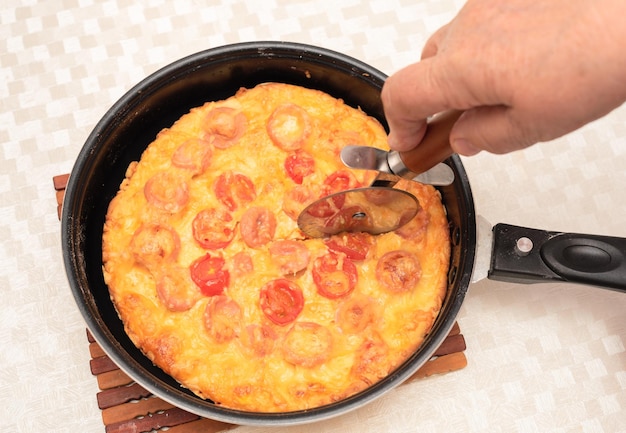 Ready to eat homemade pizza with sausages tomatoes and cheese\
being cut with a pizza cutter by senior woman hand top view with\
selective focus process of cooking pizza step 13